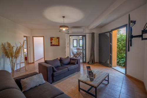 Salon moderne à la Résidence Guddelmoni à Propriano avec canapés foncés, TV écran plat, table basse en bois et vue sur le jardin