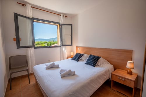 Chambre lumineuse avec lit en bois, vue sur le jardin et tables de nuit à la Résidence Guddelmoni, Propriano