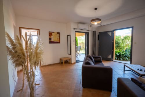 Salon moderne de l'appartement Résidence Guddelmoni avec canapé gris foncé, accès à la terrasse et vue sur le jardin à Propriano