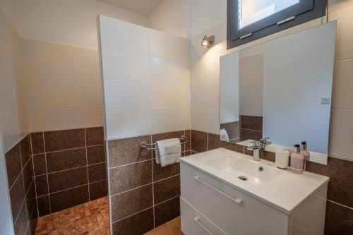 Salle de bains moderne aux carrelages marron et blanc, douche à l'italienne, meuble vasque et miroir à la Résidence Guddelmoni, Propriano