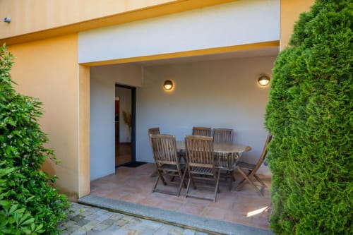 Patio de l'appartement rez-de-chaussée à la Résidence Guddelmoni à Propriano avec table de salle à manger, chaises en bois et haies verdoyantes
