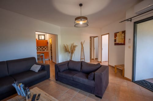 Salon moderne de l'appartement Residence Guddelmoni avec canapés sombres, luminaire suspendu et accès à la vue sur le jardin à Propriano
