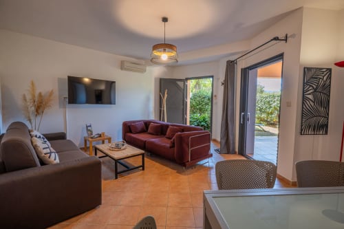 Salon moderne avec canapé bordeaux, carrelage en terre cuite et vue jardin à la Residence Guddelmoni, appartement à Propriano