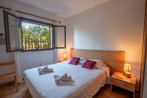 Chambre lumineuse à la Résidence Guddelmoni, Propriano avec vue sur le jardin, tête de lit en bois, coussins violets, éclairage chaleureux