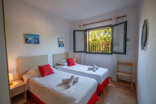 Lits jumeaux avec accents rouges dans une chambre lumineuse avec vue sur le jardin à la Résidence Guddelmoni, Propriano