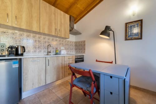 Modern kitchen and dining area with wooden cabinets, patterned tile backsplash, blue storage unit, and red chair at Quinta