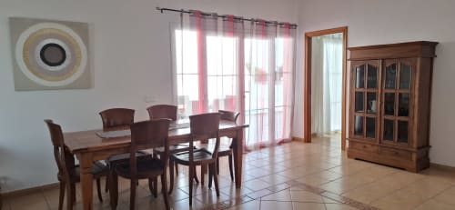 Comedor de villa moderna con muebles de madera, grandes ventanales con cortinas rosa, armario de madera y arte circular en pared