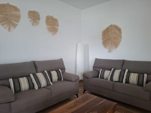 Salón de villa moderna con sofás grises, cojines a rayas y decoración de pared tejida en Puerto Calero