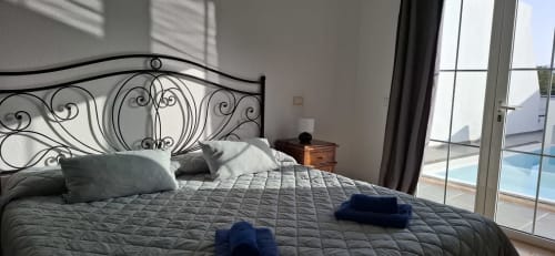 Dormitorio con cabecero de hierro forjado ornamental, vistas al mar a través de puertas de cristal que dan a la piscina en Villas del Mar, Puerto Calero