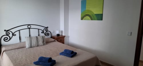 Amplio dormitorio de villa en Villas del Mar con cama de marco negro ornamentado, almohadas a rayas y toallas azules en Puerto Calero, Las