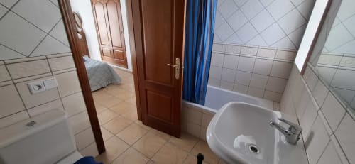 Baño moderno en Villa 6 de Villas del Mar, Puerto Calero, con lavamanos blanco, cortina de ducha azul y paredes alicatadas