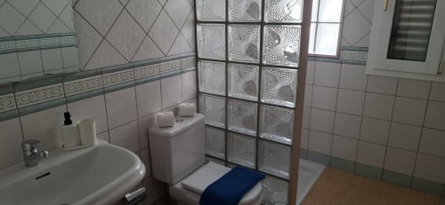 Baño moderno de la villa Villas del Mar en Puerto Calero con paredes alicatadas, inodoro, lavabo y mampara de ducha con bloques de vidrio