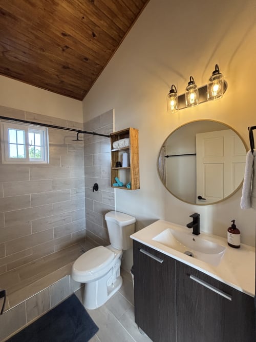 Baño moderno con ducha abierta, tocador oscuro, espejo redondo y techo de madera en BarrBra BnB en Bocas del Toro