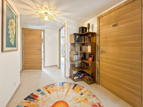 Couloir d'appartement moderne à Calvi avec portes en bois, bibliothèque, tapis soleil décoratif et lustre élégant