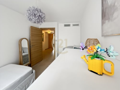 Chambre moderne de l'appartement de Calvi avec fleurs colorées sur lit blanc, porte en bois et miroir