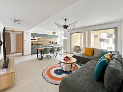 Salon moderne avec canapé gris, coin repas, cuisine équipée et vue sur la ville à Calvi, Corse