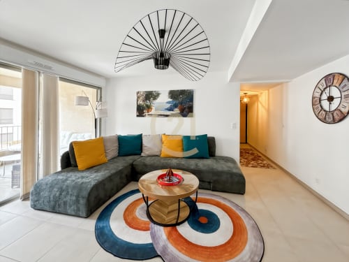 Salon moderne de l'appartement de Calvi avec canapé gris, coussins colorés, table bois et tapis géométrique