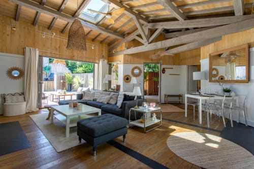 Intérieur villa moderne à La Loge Du Bassin, salon ouvert avec poutres bois, canapé anthracite, salle à manger et portes donnant sur jardin