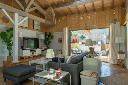 Salon moderne de la villa La Loge Du Bassin, Lège Cap Ferret, avec poutres en bois, canapé gris et vue sur le jardin