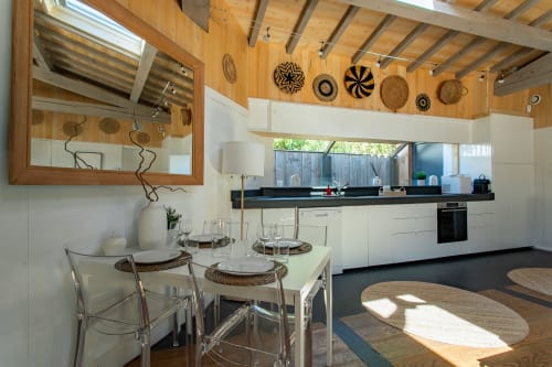Cuisine et salle à manger d'une villa moderne avec armoires blanches, plan de travail noir, plafond en bois et paniers tressés décora