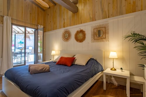 Chambre moderne de la villa La Loge Du Bassin avec literie bleue, tête de lit blanche, plafond en bois et design côtier français