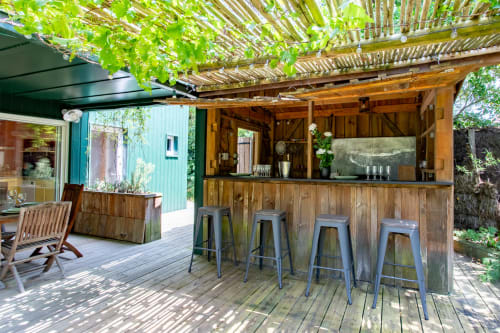 Bar extérieur avec comptoir en bois et tabourets métalliques sous pergola fleurie de vignes, Villa Cap à l'Ouest à La Loge Du Bassin