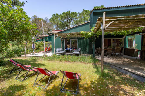 Chaises longues rouges sur la pelouse du jardin de la villa La Loge Du Bassin à Lège-Cap-Ferret, avec bâtiments verts et terrasses en bois