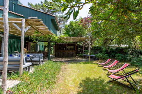 Vue du jardin de la villa La Loge Du Bassin avec transats, pergolas et espace repas extérieur à Lège-Cap-Ferret