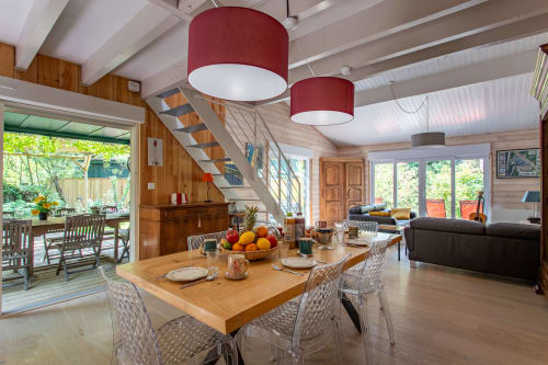 Espace ouvert salle à manger et séjour à la Villa Cap à l'Ouest à La Loge Du Bassin avec table en bois, luminaires suspendus rouges et