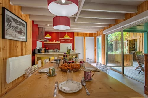 Salle à manger moderne de la villa La Loge Du Bassin avec table en bois, cuisine rouge et vue sur le jardin à Lège-Cap-Ferret
