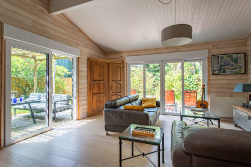 Salon de villa moderne avec sièges en cuir et vue sur le jardin depuis les portes-fenêtres à La Loge Du Bassin, Lège-Cap-Ferret