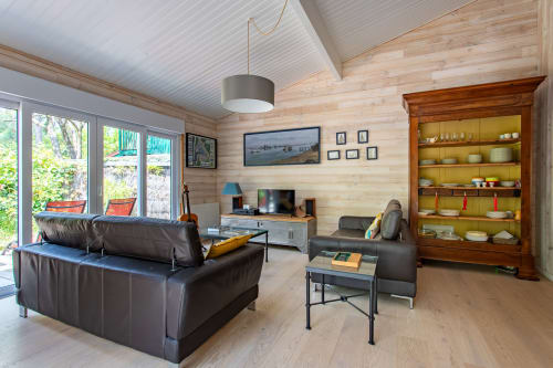 Lounge contemporain en bois avec canapé en cuir, téléviseur, étagères jaunes et vue sur le jardin à La Loge Du Bassin