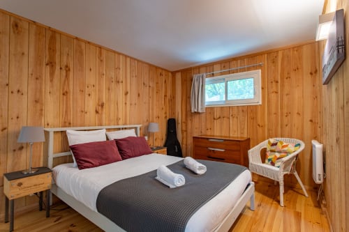 Chambre cosy en bois à la villa La Loge Du Bassin à Lège-Cap-Ferret avec lit queen, coussins bordeaux et vue jardin