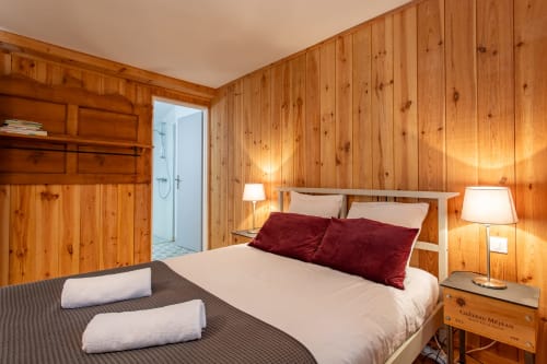 Chambre chaleureuse avec lit queen-size, oreillers bordeaux, lampes de chevet et salle de bains attenante à La Loge Du Bassin