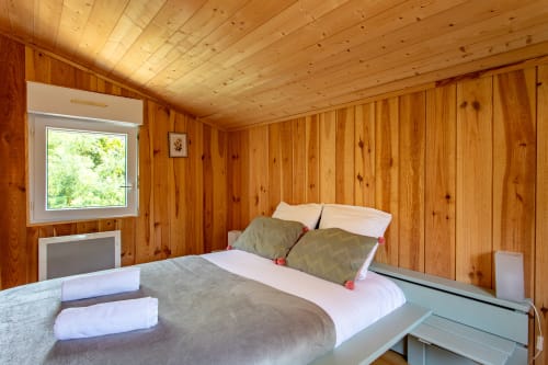 Chambre en bois à la villa La Loge Du Bassin avec lit, oreillers, serviettes blanches et vue sur le jardin