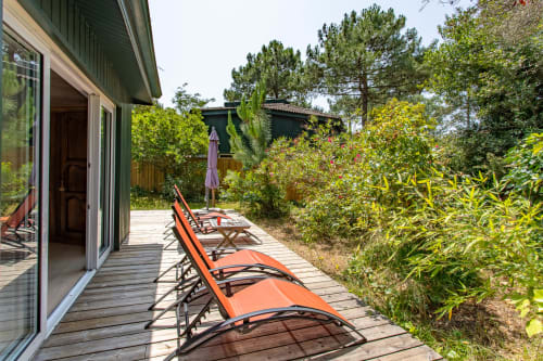 Chaises longues orange sur terrasse en bois avec vue sur jardin verdoyant à La Loge Du Bassin, Lège-Cap-Ferret