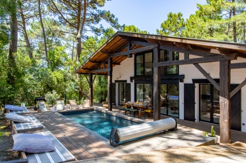 Espace piscine chauffée de la villa moderne La Loge Du Bassin à Lège-Cap-Ferret, avec terrasse en bois, chaises longues et pins