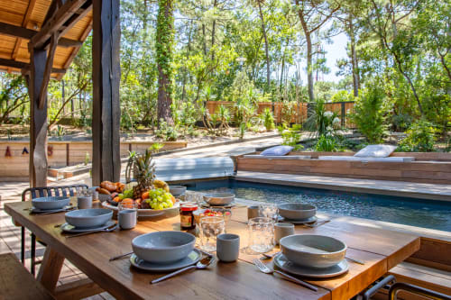 Espace repas en plein air à la villa La Loge Du Bassin avec table dressée, fruits frais, piscine chauffée et vue sur la forêt à Lège-Cap-Ferret