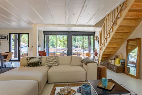 Spacieux salon de villa moderne avec canapé sectionnel crème, escalier en bois et vue sur la piscine par les grandes portes coulissantes à La