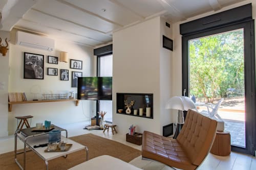 Salon moderne de la villa La Loge Du Bassin avec fauteuil en cuir beige, téléviseur, bureau et vue sur le jardin par les portes vitrées