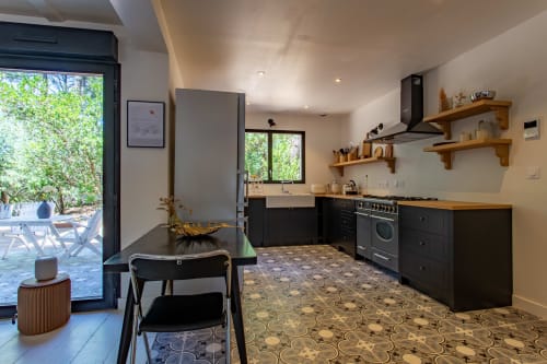 Cuisine contemporaine avec mobilier noir, étagères en bois et sol décoratif à la villa La Loge Du Bassin, Lège-Cap-Ferret