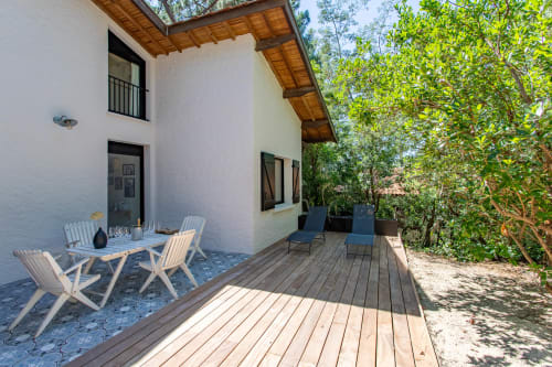 Terrasse de la villa La Loge Du Bassin avec deck en bois, chaises longues blanches, table à manger et vue sur le jardin luxuriant à Lège-Cap-Ferret