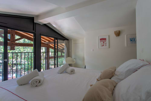 Chambre lumineuse avec literie blanche, serviettes roulées et accès au balcon surplombant la piscine de la villa La Loge Du Bassin
