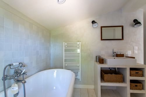Salle de bain moderne avec baignoire autoportante blanche, vasque, paniers de rangement tressés et miroir encadré à La Loge Du Bassin