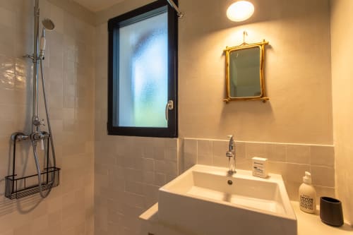 Salle de bain moderne avec vasque carrée blanche, miroir cadre doré, douche et fenêtre en verre texturé à la villa Pins d'Agalis