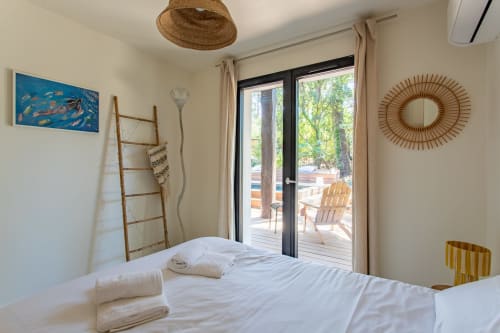 Chambre lumineuse aux draps blancs, décoration d'échelle en bois, portes vitrées donnant sur une terrasse avec fauteuils Adirondack à La Loge Du