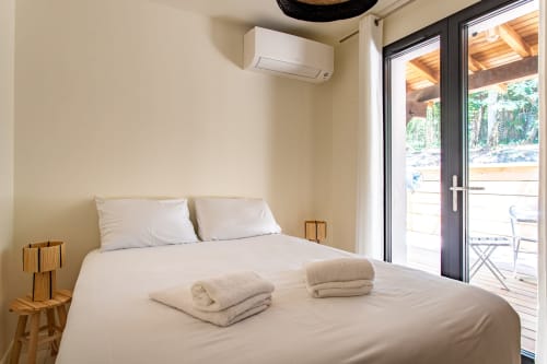 Chambre moderne avec literie blanche, serviettes enroulées, climatisation, tables de nuit en bois, portes vitrées vue piscine