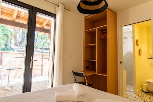 Chambre moderne à la villa La Loge Du Bassin avec armoire en bois, lit, portes vue piscine et salle de bain attenante aux accents jaunes