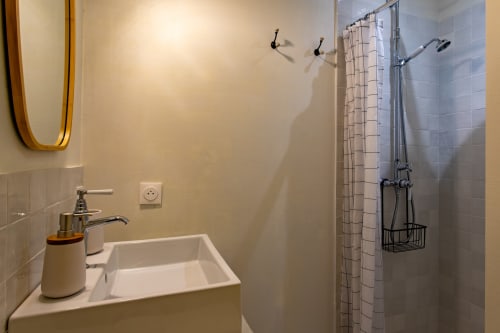 Salle de bain moderne avec lavabo blanc, distributeur de savon, rideau de douche à carreaux et accessoires noirs à La Loge Du Bassin