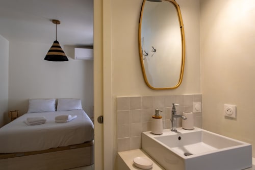 Salle de bain moderne avec lavabo blanc, miroir doré et chambre adjacente à la villa La Loge Du Bassin à Lège-Cap-Ferret